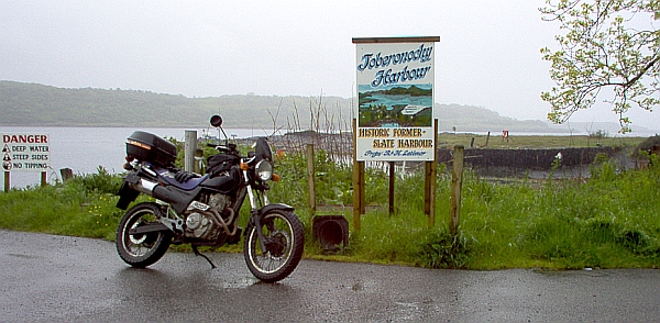 my bike next to a sign saying toberonochy harbour in the rain